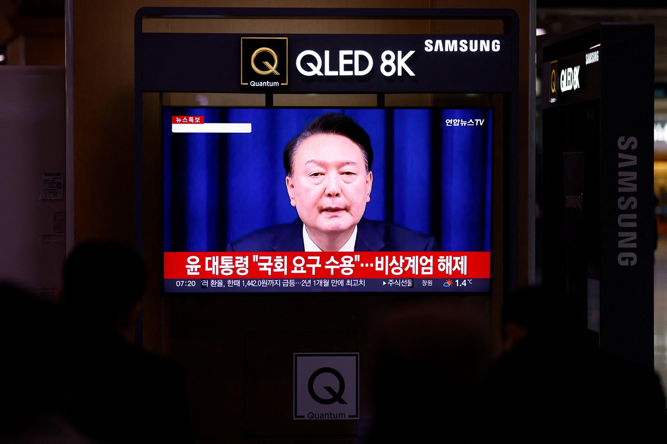 People at a railway station in Seoul watch a news report on President Yoon Suk Yeol's lifting of...