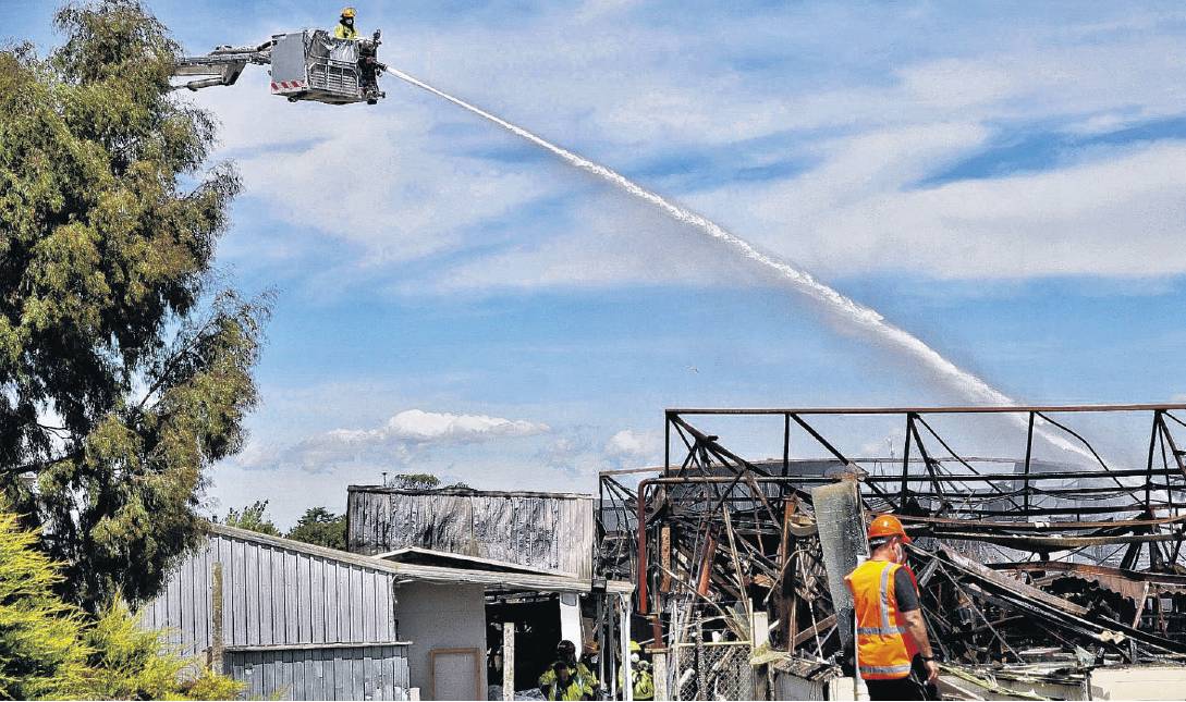 A Fire and Emergency New Zealand crew member hosing water onto the remains of the old Sutton...