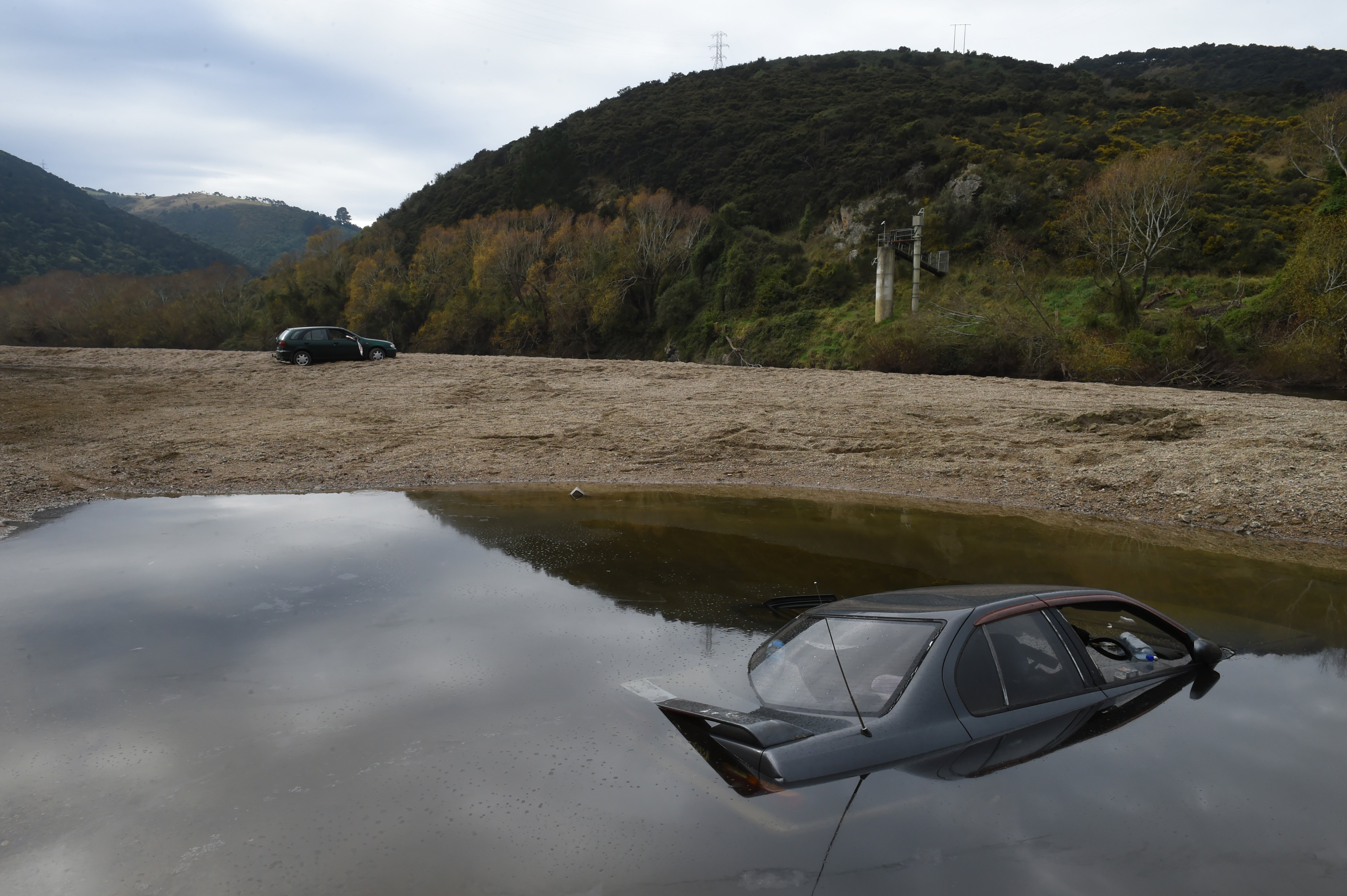 A Nissan Primera sits on the bed of the Taieri River,  and a Nissan Sentra lies abandoned at...