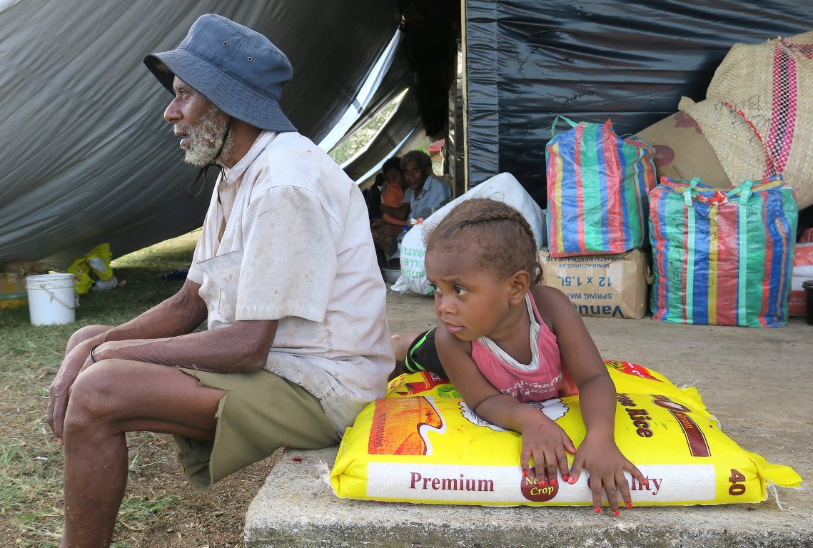 Residents evacuated from Ambae sit near their possessions and food supplies at an evacuation...