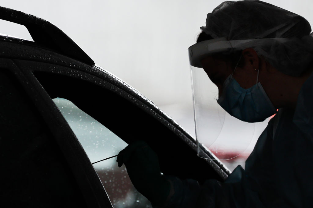 A nurse wearing a face-shield conducts a Covid-19 test at a drive-through testing facility in...