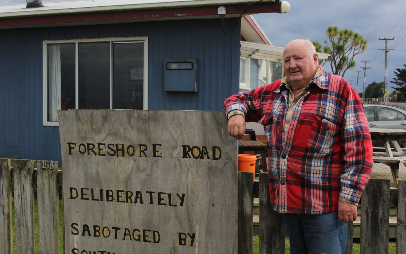 Kevin Mulqueen leans against a sign he attached to the fence of his Colac Bay home. Photo: LDR /...