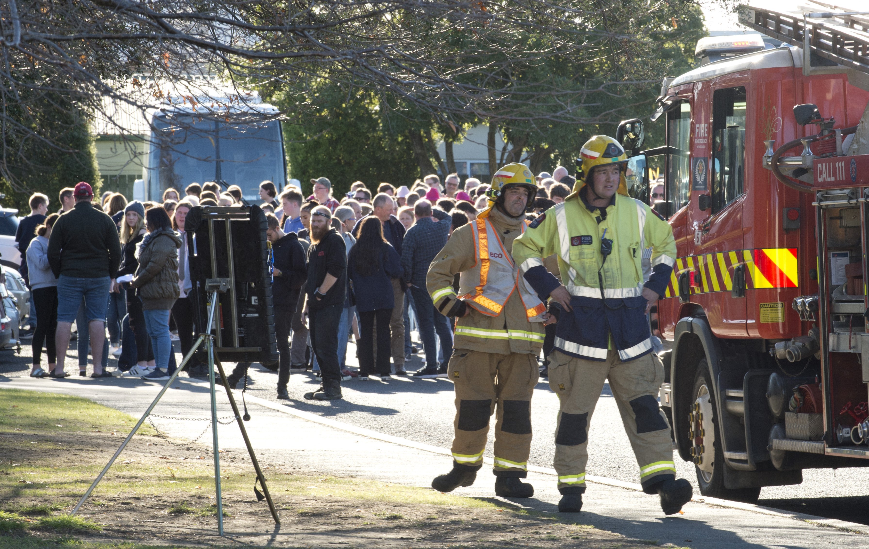 Firefighters assess the cause of a fire alarm while the crowd gathers outside Taieri College....