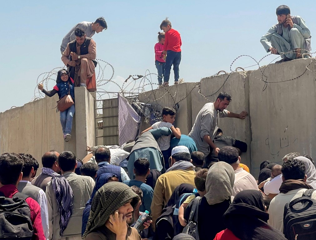 A man pulls a girl up a wall as they try to to get inside Hamid Karzai International Airport in...