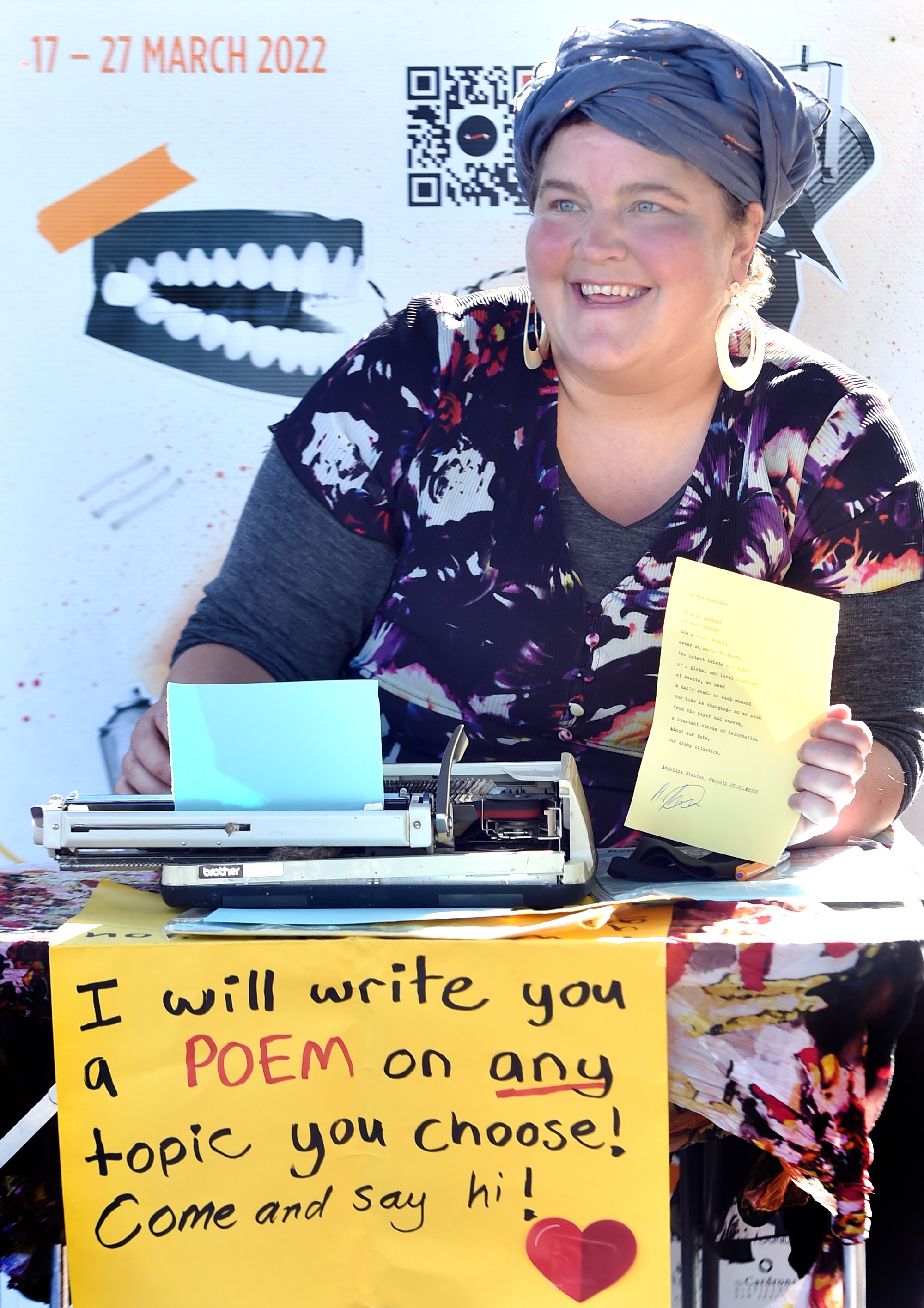 Street poet Angelina Stanton holds up her poem titled To The Readers written in the Octagon...