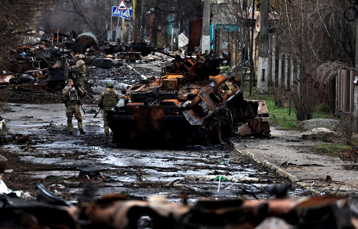 A soldier takes a photograph of his comrade as he poses beside a destroyed Russian tank and...