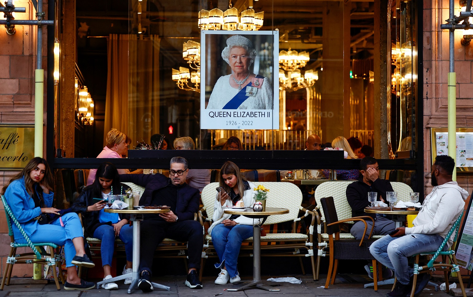 People sit outdoors under an image of Britain's Queen Elizabeth in London on Saturday. Photo:...