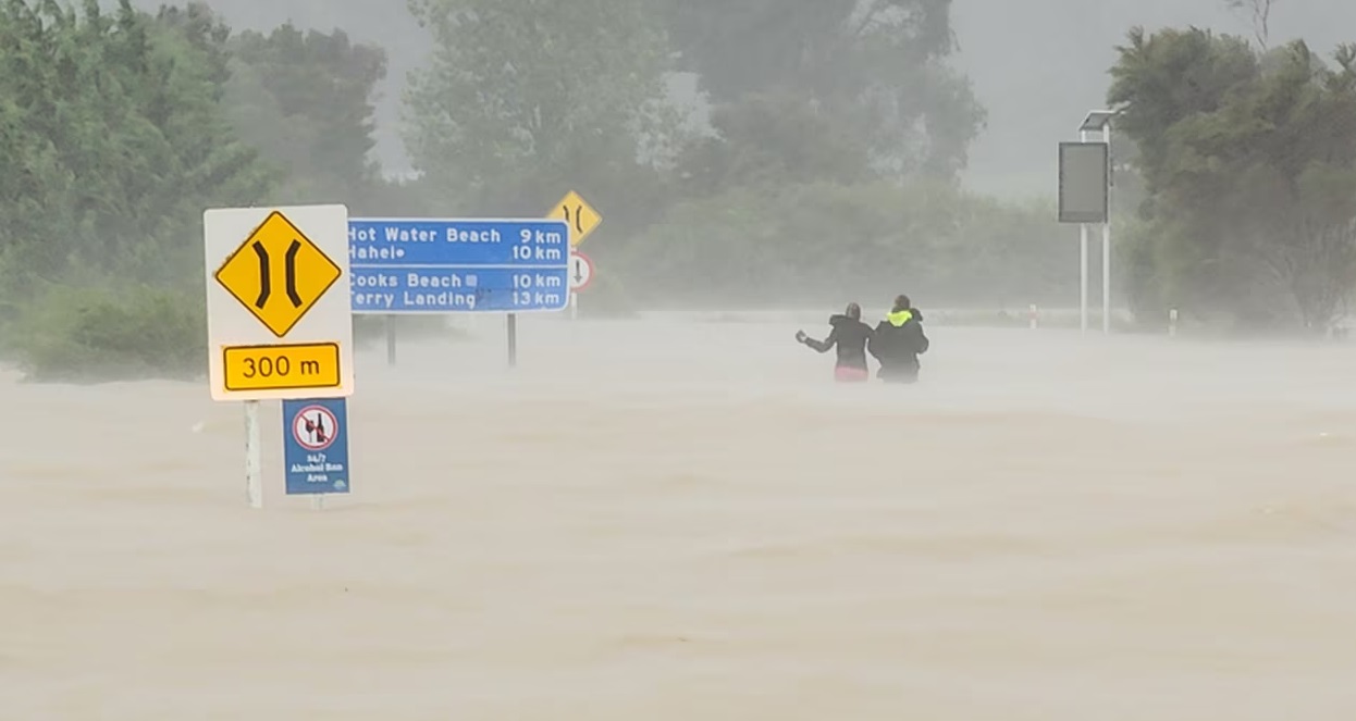 Two people wade through waist-high water after abandoning their car on the road to Hahei on the...