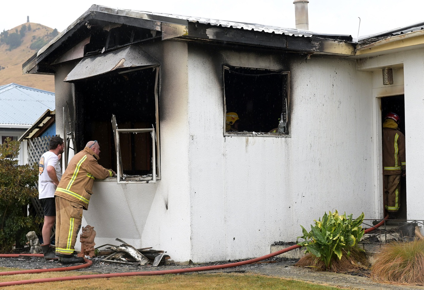 Firefighters and a neighbour inspect the damage.