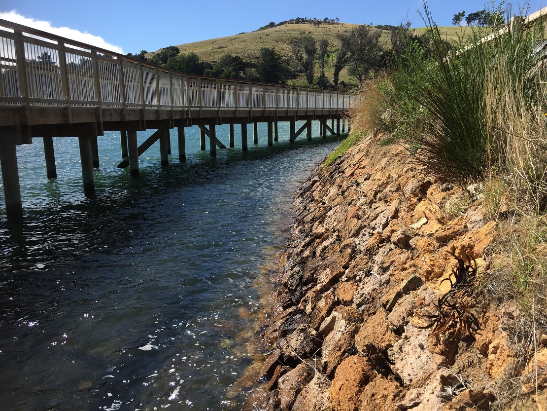 A boardwalk swings out past a section of old stone wall.