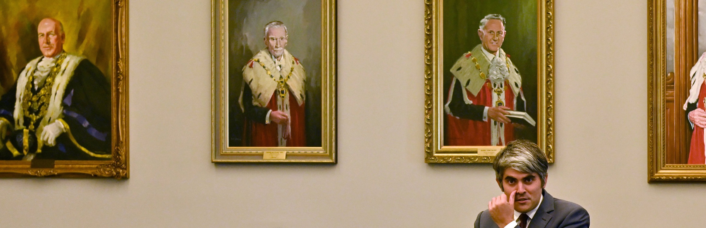 Former Dunedin Mayor Aaron Hawkins sits in front of mayoral portraits of early Dunedin mayors....