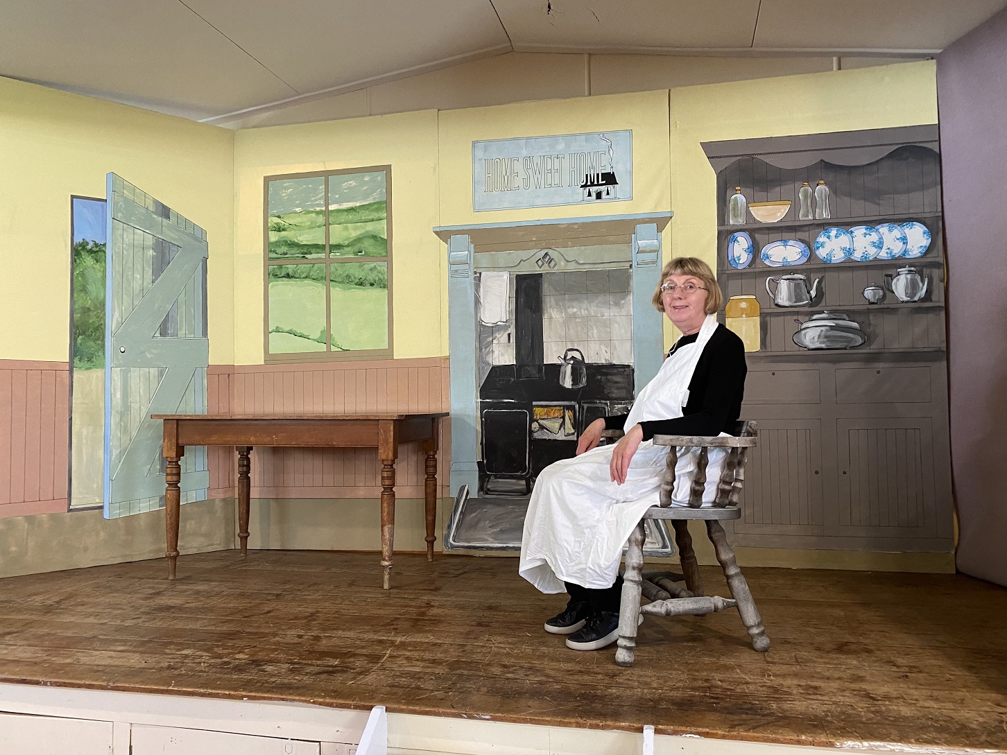 Tessa Mills sits against a backdrop depicting a 19th century cottage, painted by Vic Mills, at...