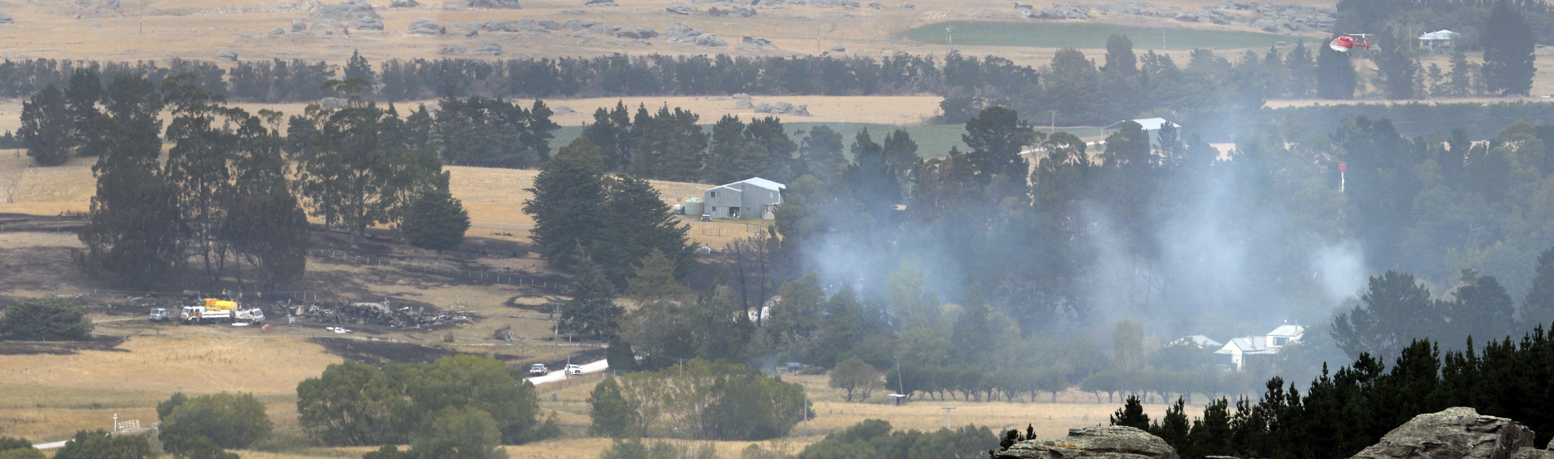 A helicopter using a monsoon bucket (right) drops water on a fire threatening a structure in...