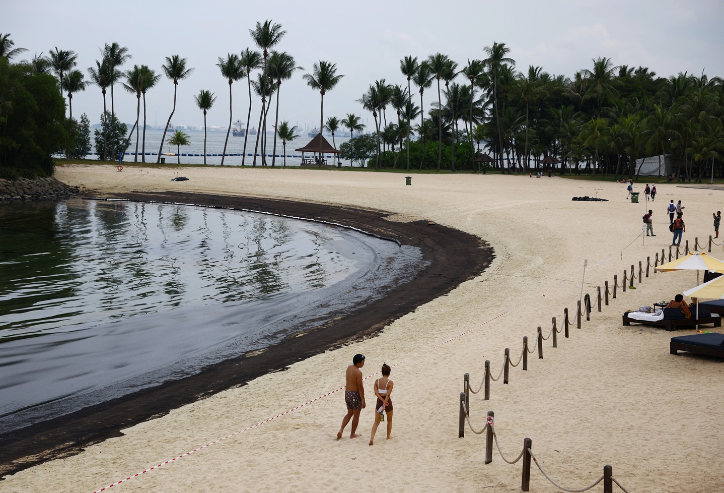 People walk next to an oil slick at Tanjong Beach on Sentosa, Singapore. Photo: Reuters