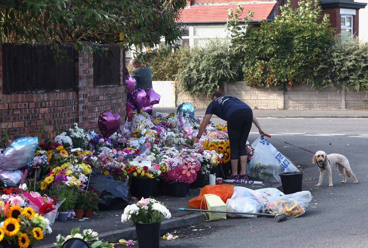 A woman arranges flowers at a makeshift memorial in Southport allowing people to pay their...