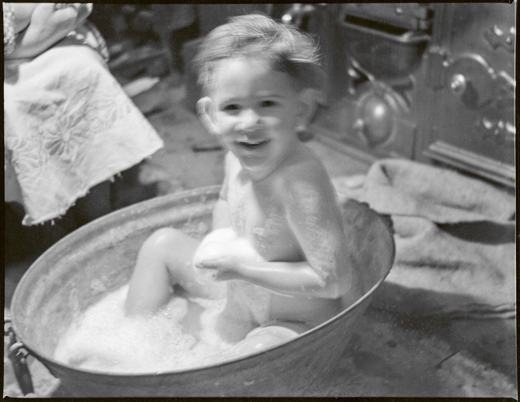 A boy sits in a tin bath in front of the kitchen range, probably at the Burrell family farm,...