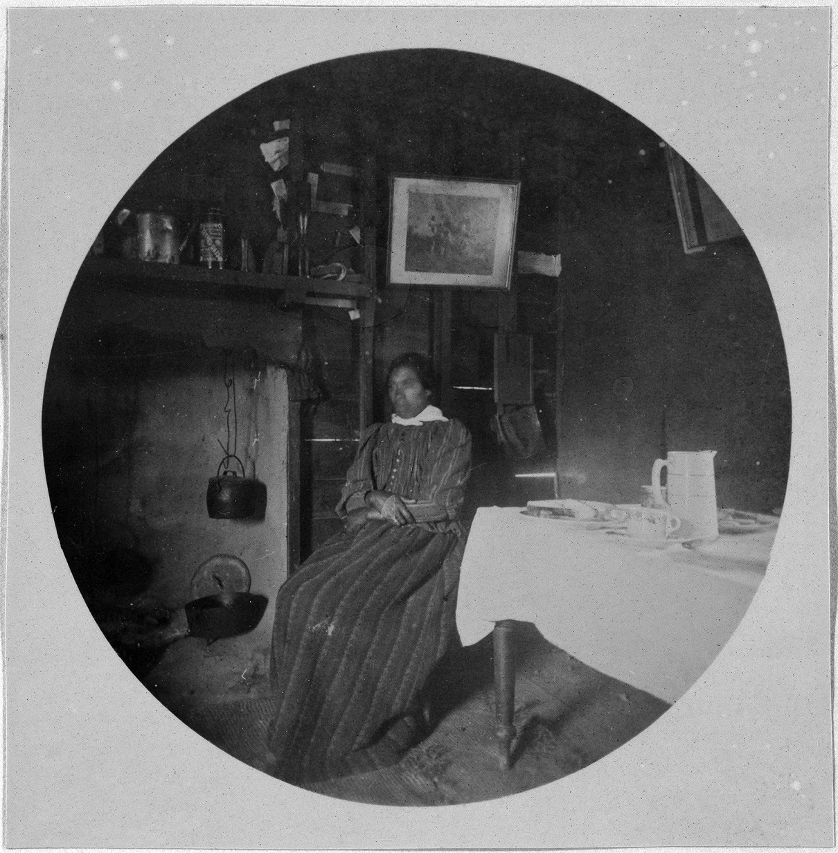 Mrs Karetai, at Ōtākou, in 1893. Mrs Karetai sits in front of the open fire, with a camp oven and...