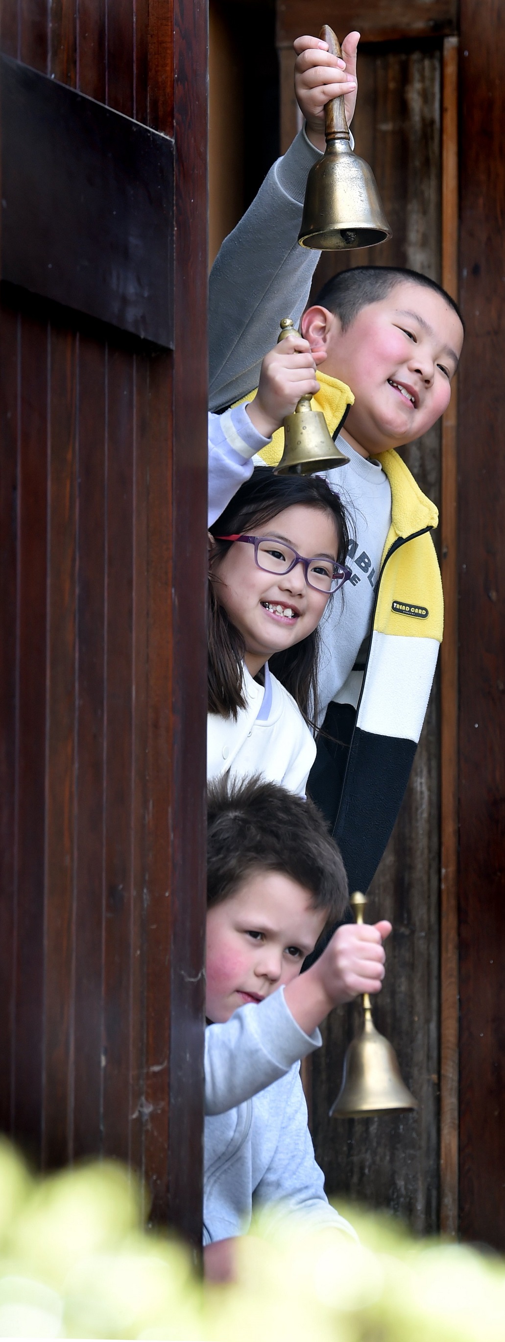 Opoho School pupils (from top) Aaron Li, 8, Chloe Xu, 8, and Oscar Bunce, 7, ring a bell...