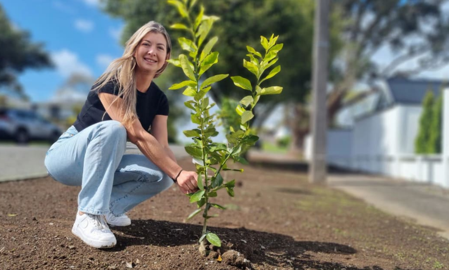 Alana Brough with one of the trees she has planted in the berm. Photo: RNZ