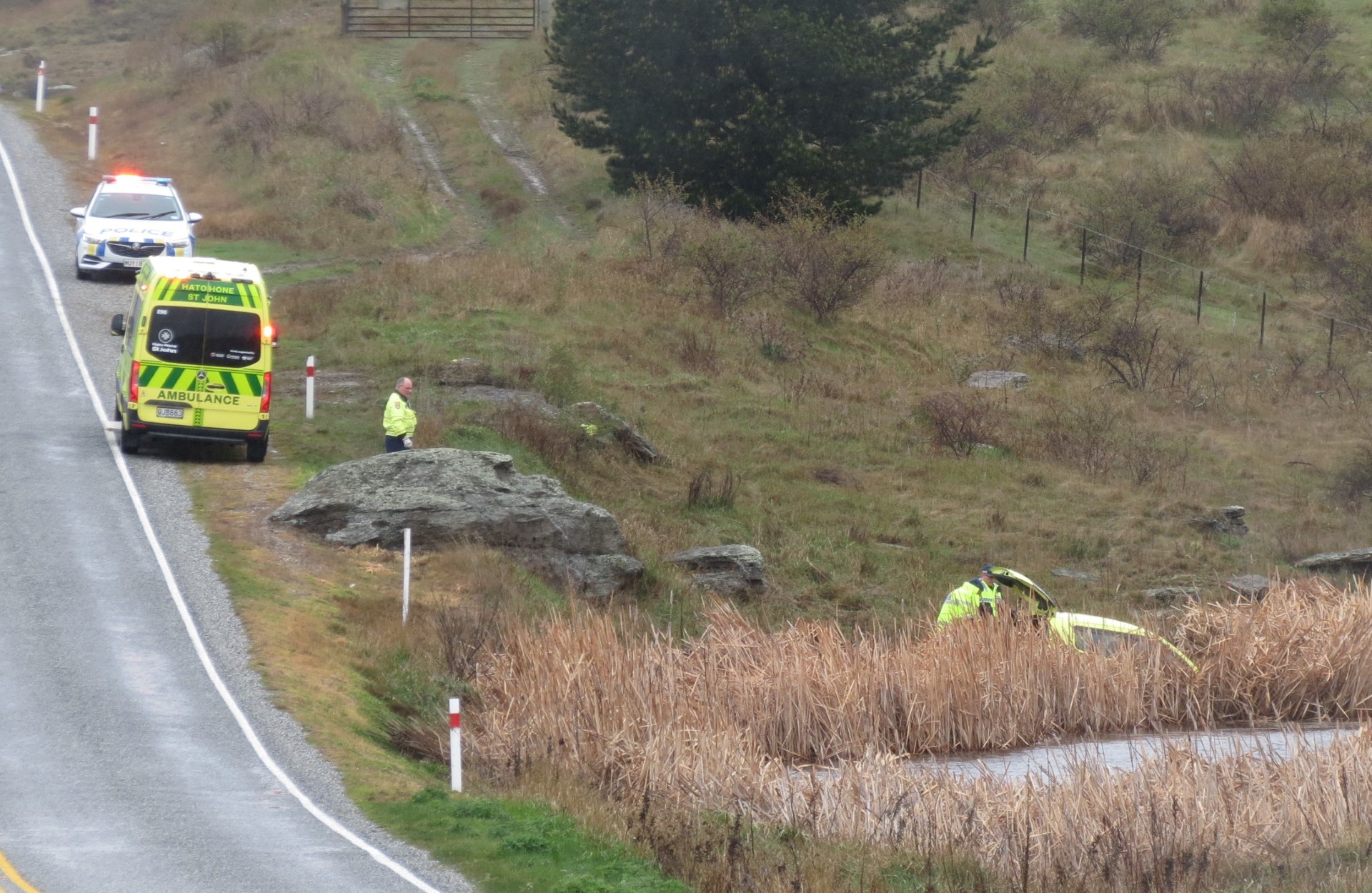 Emergency services inspect a car which went off the road south of Alexandra today. PHOTO: RUBY SHAW