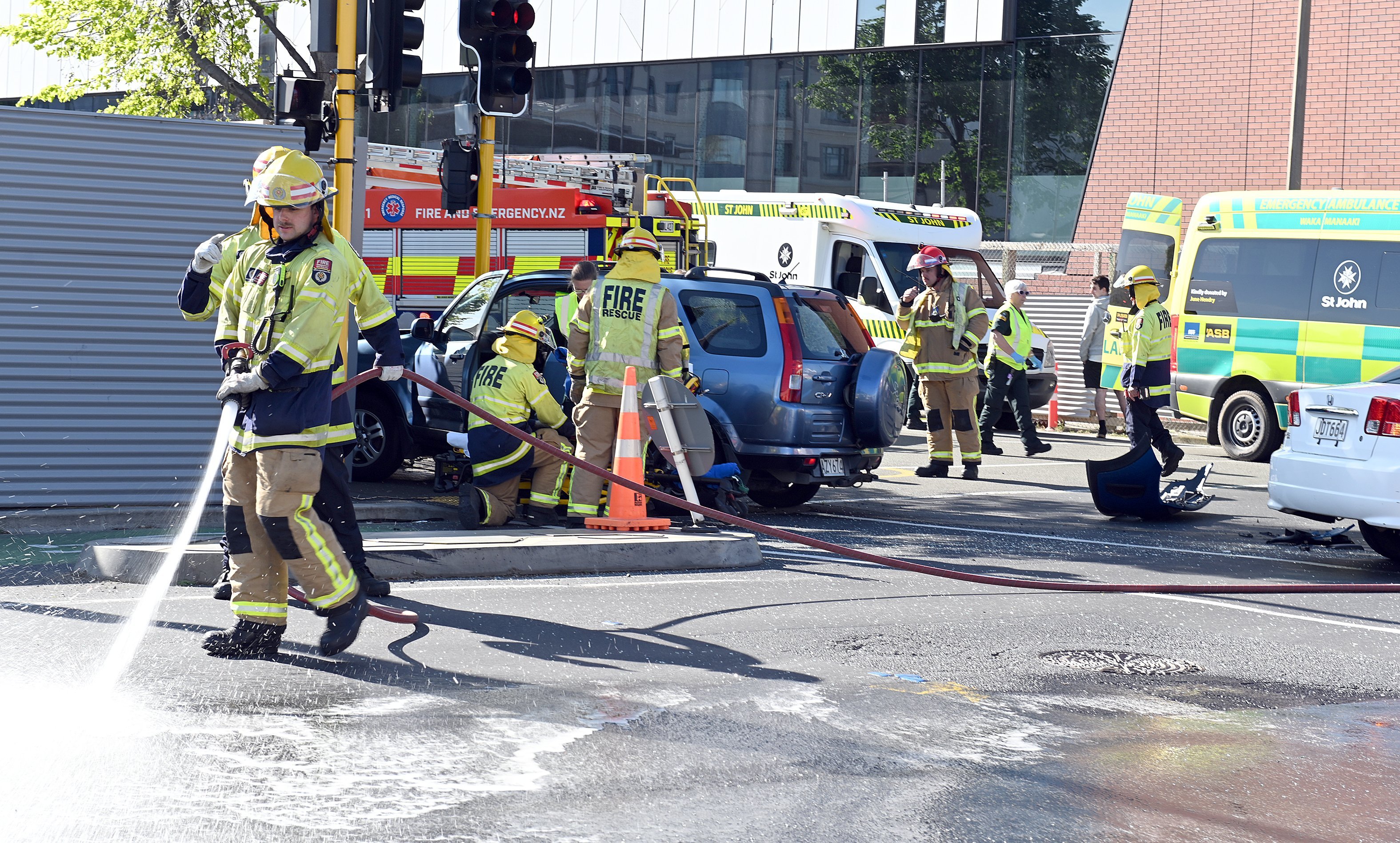 A firefighter washes debris from the road as a person is extricated from a car after the crash at...