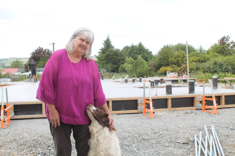 Excitement builds ... Raelene Burr pats her dog Ollie in front of the new house being built on...