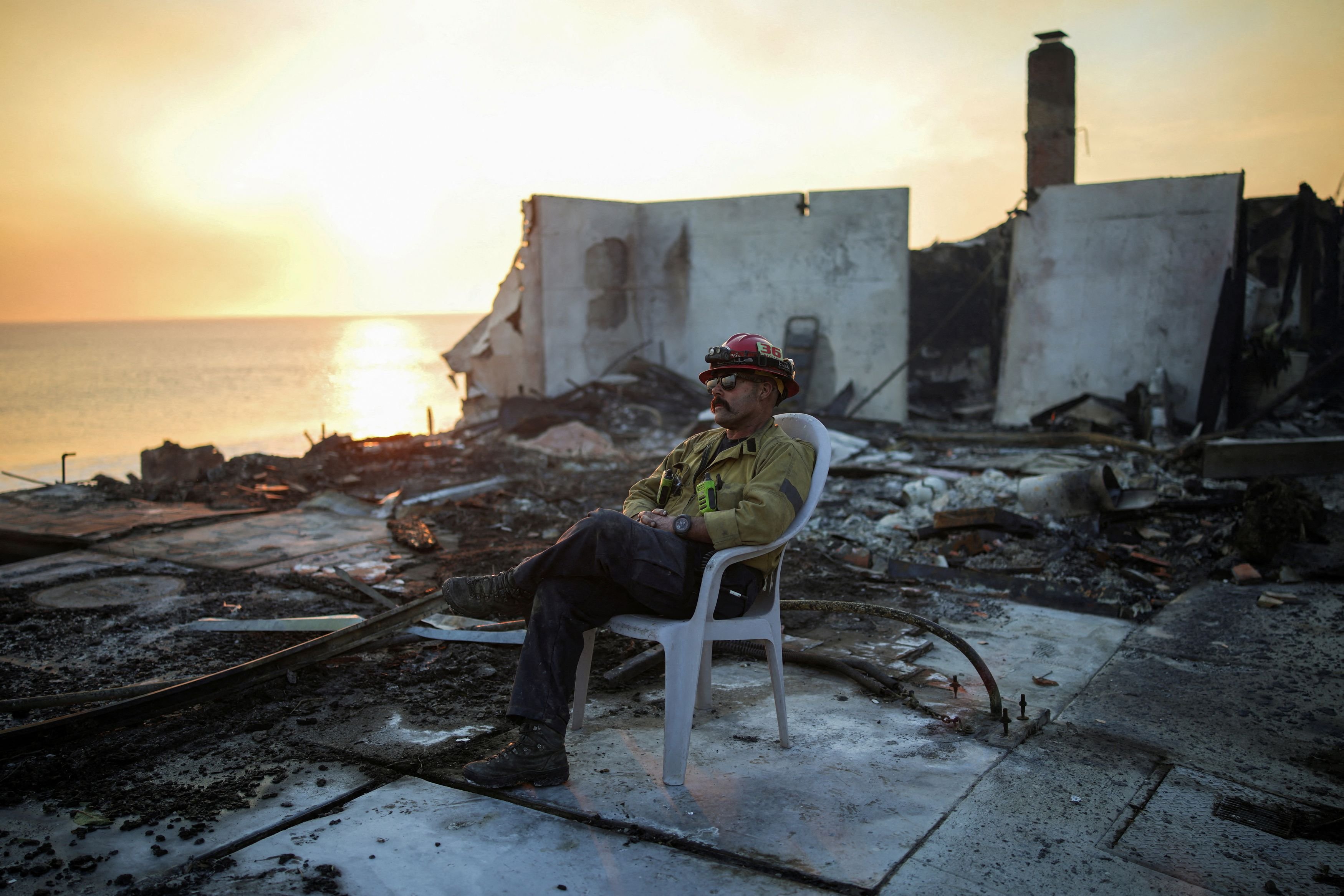 A firefighter sits on a chair amid the remains of a burnt structure along the Pacific Coast...