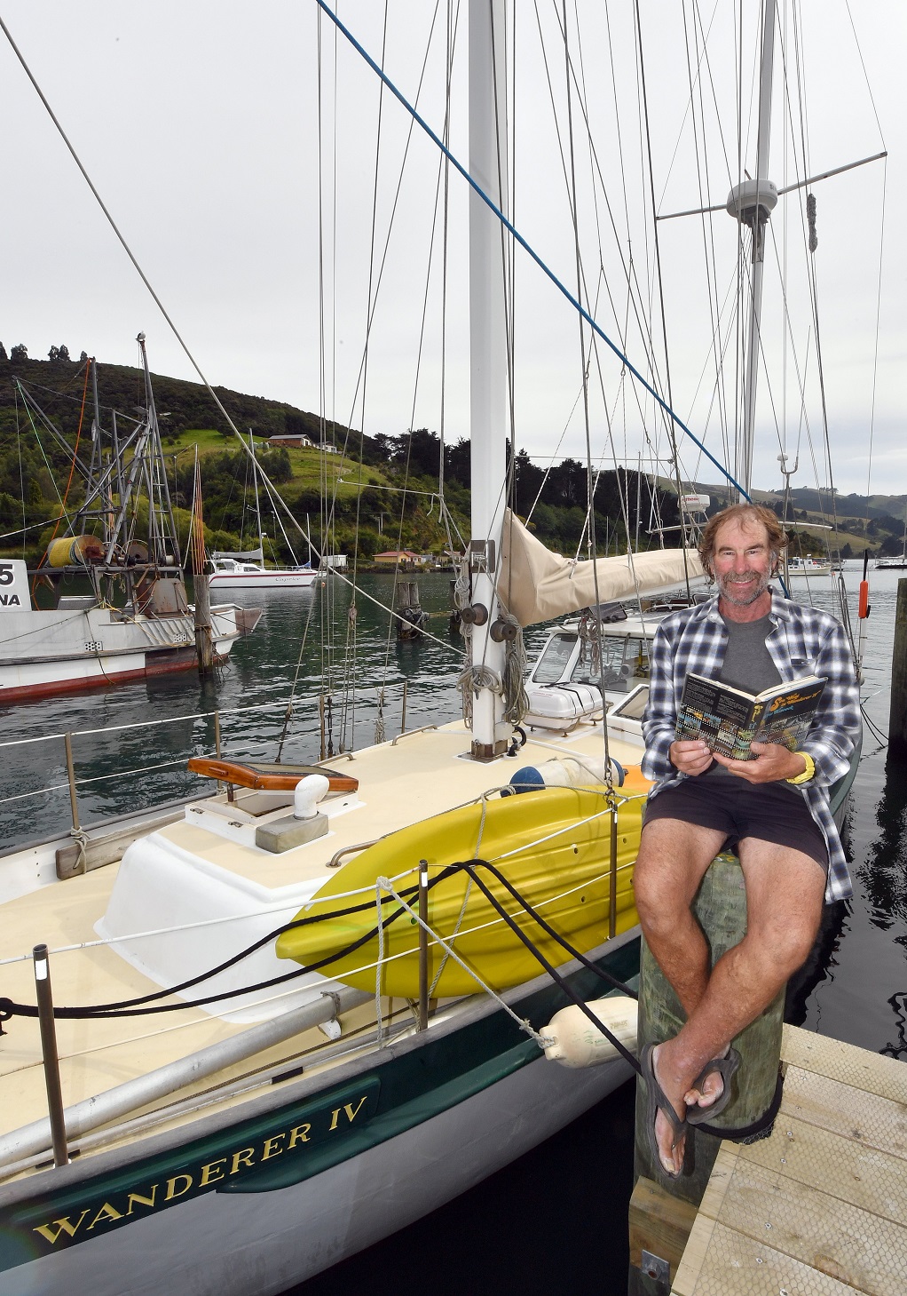 Trevor Whelan sits beside his yacht Wanderer IV  as he reads a cruising book, Sou’West in...