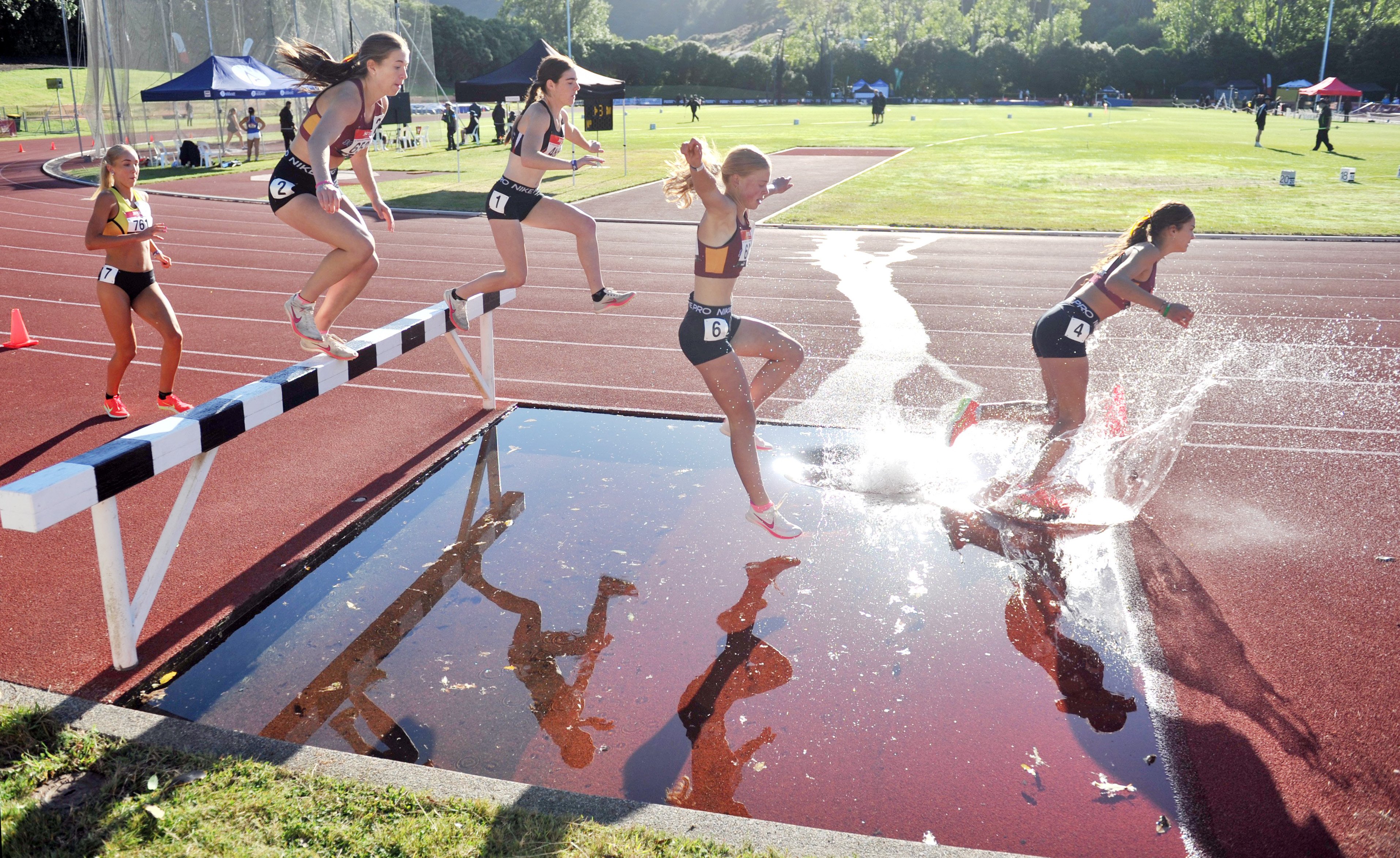 Rising stars clear the hurdle and run through the water during the women's under-18 steeplechase...