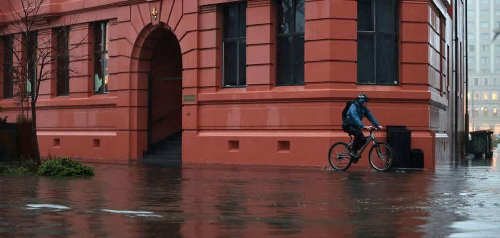 A cyclist makes their way through flooded waters near the Avon River. Photo / George Heard