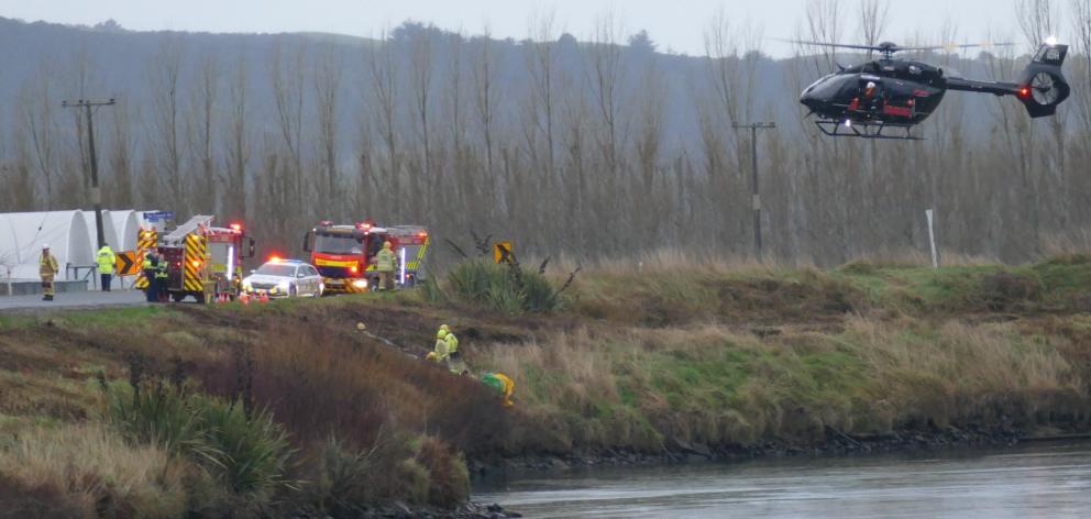 Emergency services personnel tend to a crash victim in his car (obscured) on the Clutha riverbank...