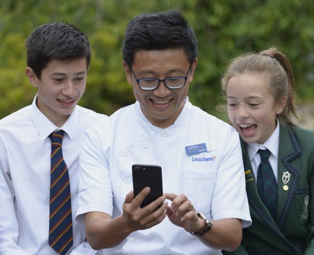 Roslyn Pharmacy owner Andrew Hou, holds a smartphone, watched by son Josh and daughter Ella. PHOTO: GERARD O’BRIEN