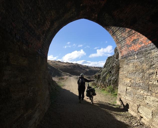 A cyclist walks her bike through a tunnel in the Poolburn Gorge on the Otago Central Rail Trail....