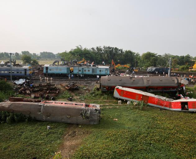 Heavy machinery removes damaged coaches from the railway tracks at the site of a train collision...