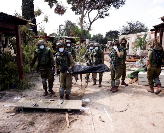 Israeli soldiers carry the body of a victim of an attack by militants from Gaza at Kibbutz Kfar...