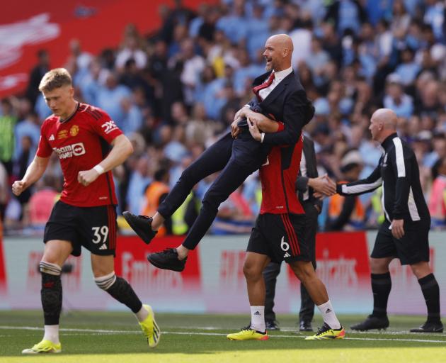 A jubilant Manchester United manager Erik ten Hag is picked up by Lisandro Martinez (obscured). ...