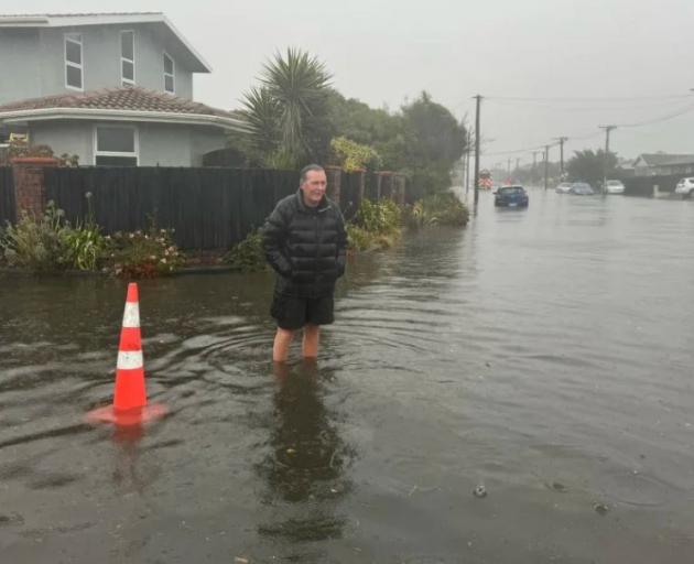 A New Brighton resident stands in floodwaters on the corner of Marine Pde and Pacific Rd on...