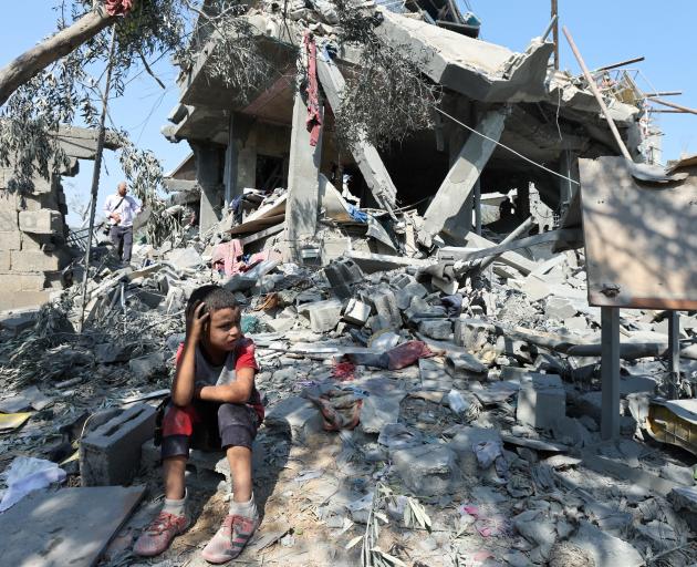 A child sits amid the rubble as Palestinians inspect a house destroyed in an Israeli strike in...