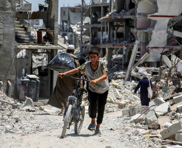 A Palestinian youth pushes a bicycle as he walks past the rubble of houses destroyed during the...