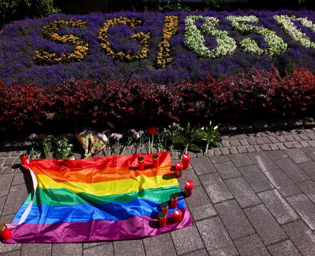 Flowers, candles and a rainbow flag are placed in front of an arrangement of flowers related to...