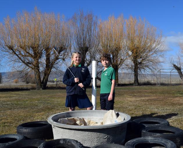 Practising chipping golf balls into a water trough on their school grounds in preparation for an...