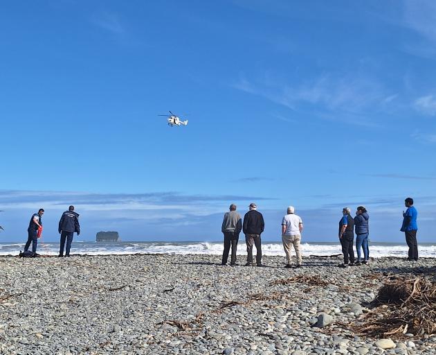 Police and onlookers watch as a rescue helicopter flies over Rapahoe Beach, where a man drowned...