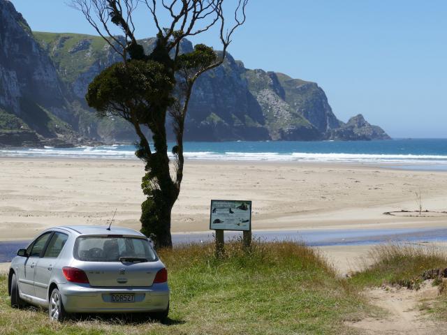 A car sits next to a sea lion advisory sign in the Pūrākaunui Beach car park in the Catlins...