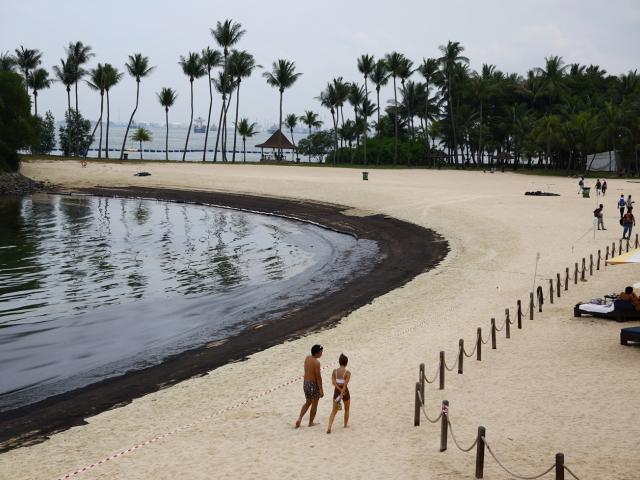 People walk next to an oil slick at Tanjong Beach on Sentosa, Singapore. Photo: Reuters