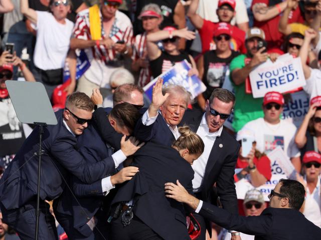 Donald Trump gestures with a bloodied face while he helped off stage after an assassination...