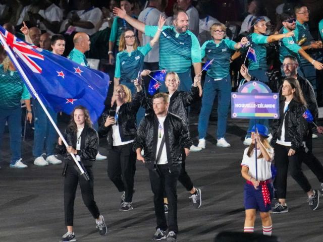 Anna Grimaldi and Cameron Leslie, flag bearers of Team New Zealand, hold their national flag as...