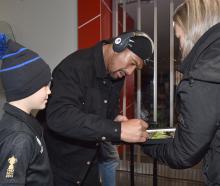 All Black loose forward Ardie Savea signs a photograph for young fan Zac Calvert, 9, and his...