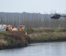Emergency services personnel tend to a crash victim in his car (obscured) on the Clutha riverbank...