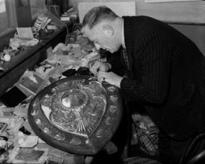 A man repairs a damaged panel on the Ranfurly Shield in this undated photograph.