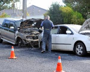 A Dunedin police photographer records the damage to two vehicles whose interiors were burned out...